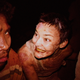 A blood spattered woman grins at a man who looks suspiciously at the camera